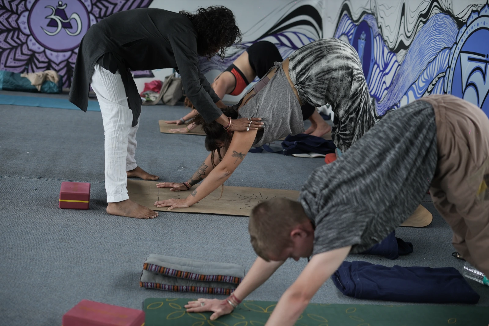 Students in a forward-fold pose with hands-on teacher adjustment